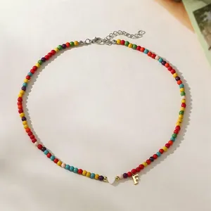 Detailed view of colorful bead necklace with white heart and gold initial F charm
