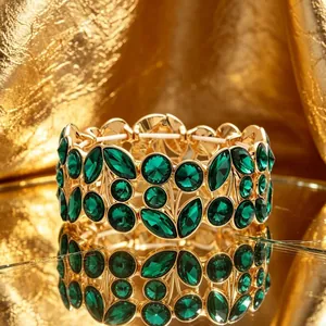 Close-up of vintage wide gold bracelet with green leaf-shaped crystals on gold background