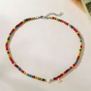 Detail view of a colorful turquoise seed bead necklace featuring heart and gold 'L' letter charms