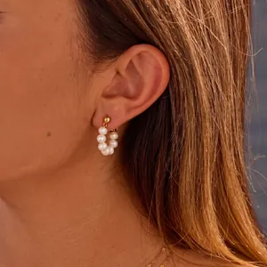 Detalle de pendientes de aro en C dorados con perlas naturales de agua dulce en la modelo