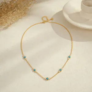Elegante collar de acero dorado con turquesa y circón sobre fondo texturizado.