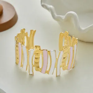 Primo piano di un bracciale rigido dorato con barre verticali in smalto bianco e rosa.