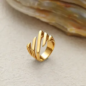 Gros plan d'une bague géométrique en acier inoxydable doré au design de feuille fluide.