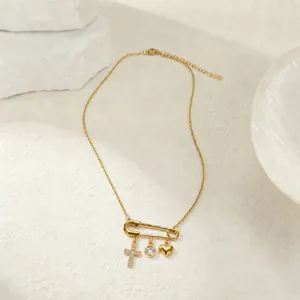 Vista detallada de un collar imperdible dorado con dijes de cruz, cristal y corazón
