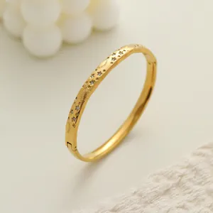 Primer plano de brazalete de acero inoxidable chapado en oro con estrellas y cristales.