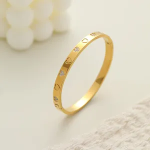 Primer plano de un brazalete de acero dorado con corazones grabados y con diamantes.