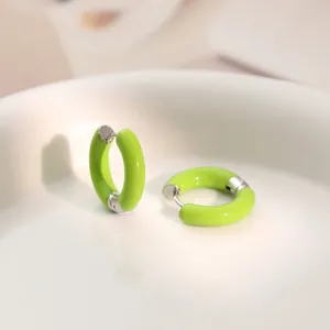 Macro view of bright green enamel C-shaped hoop earrings on white ceramic plate