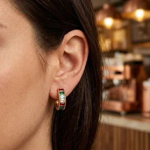 Primer plano de pendientes de aro dorados con circonitas de colores talla baguette