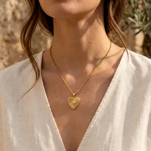Close-up detail of a gold heart pendant necklace with textured pattern on a model