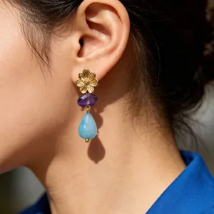 Detail van gouden bloemenoorbellen met paarse en blauwe natuurstenen aan het oor