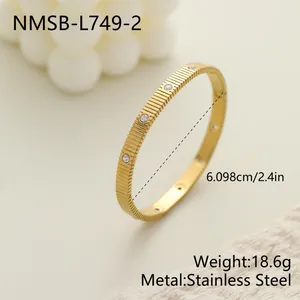Detalle de brazalete de acero inoxidable dorado con textura acanalada y piedras