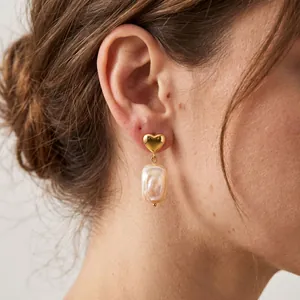 Gros plan d'une boucle d'oreille cœur en or avec une perle baroque naturelle pendante