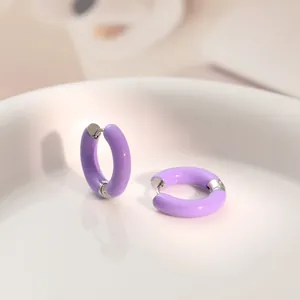Macro view of vibrant purple dopamine-style enamel hoop earrings on a white ceramic tray