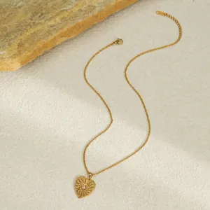 Detailed view of a gold-plated textured heart pendant necklace on a stone background.