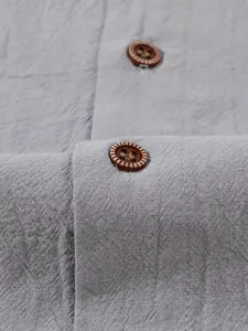 Macro detail of grey linen fabric and brown decorative button on a men's casual shirt