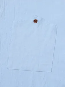 Close-up detail of a light blue linen shirt pocket featuring a classic brown button.