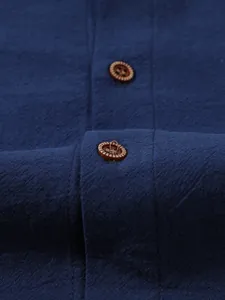 Close-up detail of dark blue linen shirt with wooden texture buttons and fabric weave.