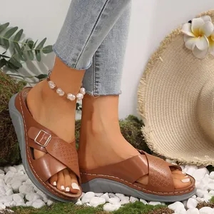 Detail view of brown wedge sandals with crisscross straps and buckle on white stones.