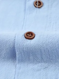 Macro close-up detail of a textured brown button on a light blue linen casual shirt