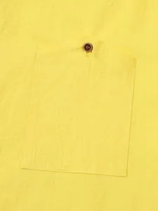 Close-up detail of yellow linen shirt pocket with brown button for men's casual wear