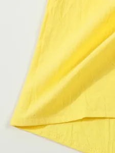 Close-up detail of yellow linen shirt fabric showing high-quality texture and hem stitching