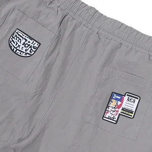 Détail du pantalon gris avec poches arrière et patchs graphiques de style streetwear.