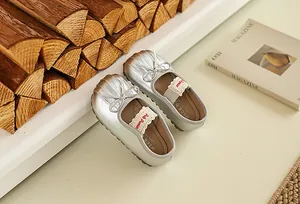 Gros plan de chaussures Mary Jane argentées pour bébé avec nœud et dentelle sur fond blanc
