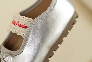 Gros plan d'une chaussure Mary Jane argentée pour filles avec texture cuir et dentelle.