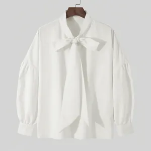 Detail view of a white loose-fit long sleeve shirt with a stylish decorative bow-tie neck