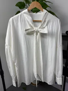 Detailed view of white loose long sleeve shirt featuring a prominent front bow tie