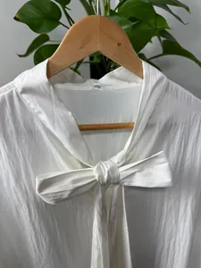 Close-up of a white men's loose shirt featuring a stylish front bow-tie design