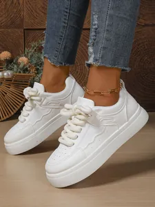 Primo piano di sneaker bianche con plateau da donna con lacci spessi e cavigliera dorata
