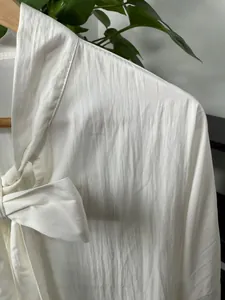 Detail view of a white long-sleeved shirt with elegant bow-tie collar and textured fabric.