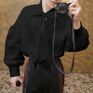 Detail view of men's black loose long-sleeved shirt with tie neck and lantern sleeves