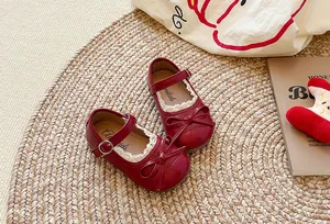 Scarpe Mary Jane rosse da bambina con pizzo e fiocco decorativo su tappeto di paglia