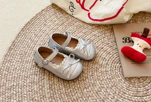 Scarpe Mary Jane argento per bambine con pizzo e fiocco su un tappeto intrecciato