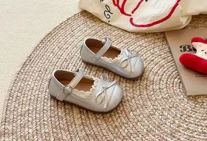 Primo piano di scarpe Mary Jane argento per bambina con pizzo e fiocco su stuoia.