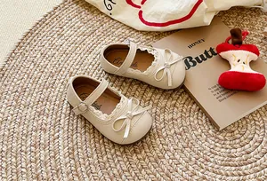 Dettaglio di scarpe Mary Jane beige per bambine con pizzo delicato e grandi fiocchi.