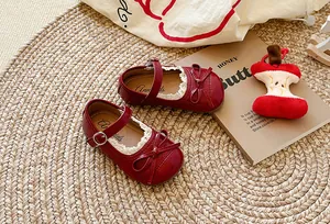 Dettaglio di scarpe Mary Jane rosse per bambina con pizzo raffinato e fiocco decorativo.