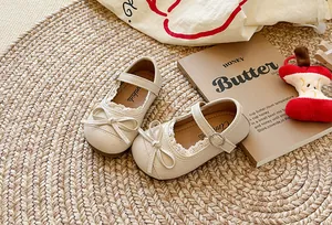 Dettaglio delle scarpe Mary Jane beige per bambine con fiocco e pizzo su stuoia