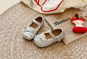 Scarpe Mary Jane argento per bambine con bordo in pizzo e fiocco decorativo su un tappeto di paglia
