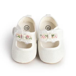 Close-up of white mesh infant shoes with delicate floral bow detail and velcro strap.
