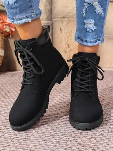 Close-up of black lace-up Martin boots worn with denim jeans on a woven rug.