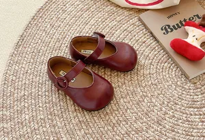 Burgunderrote Mary Jane Lederschuhe für Kinder mit Schnalle auf einer runden Strohmatte.