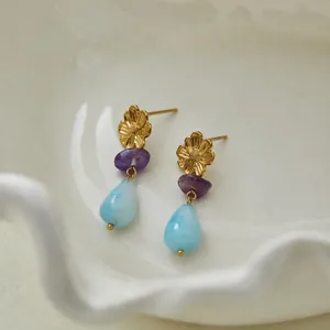 Detailopname van gouden bloem oorknopjes met paarse en blauwe natuurlijke stenen hangers.