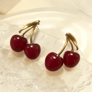 Close-up of retro enamel cherry earrings with glossy red finish and golden leaves