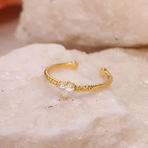 Gros plan d'une bague torsadée dorée avec un zircon en forme de cœur sur une roche blanche