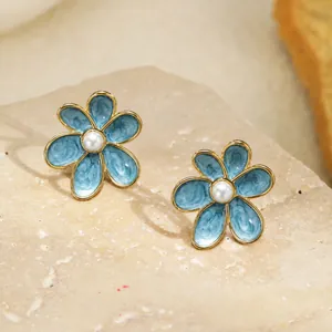 Vue macro de boucles d'oreilles fleur émail bleu avec perles élégantes sur support pierre