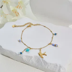 Detailansicht eines vergoldeten Edelstahlarmbands mit blauer Blume und Vogelanhängern.