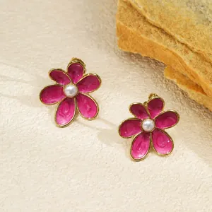 Gros plan détaillé des boucles d'oreilles fleurs en émail magenta avec une perle au centre